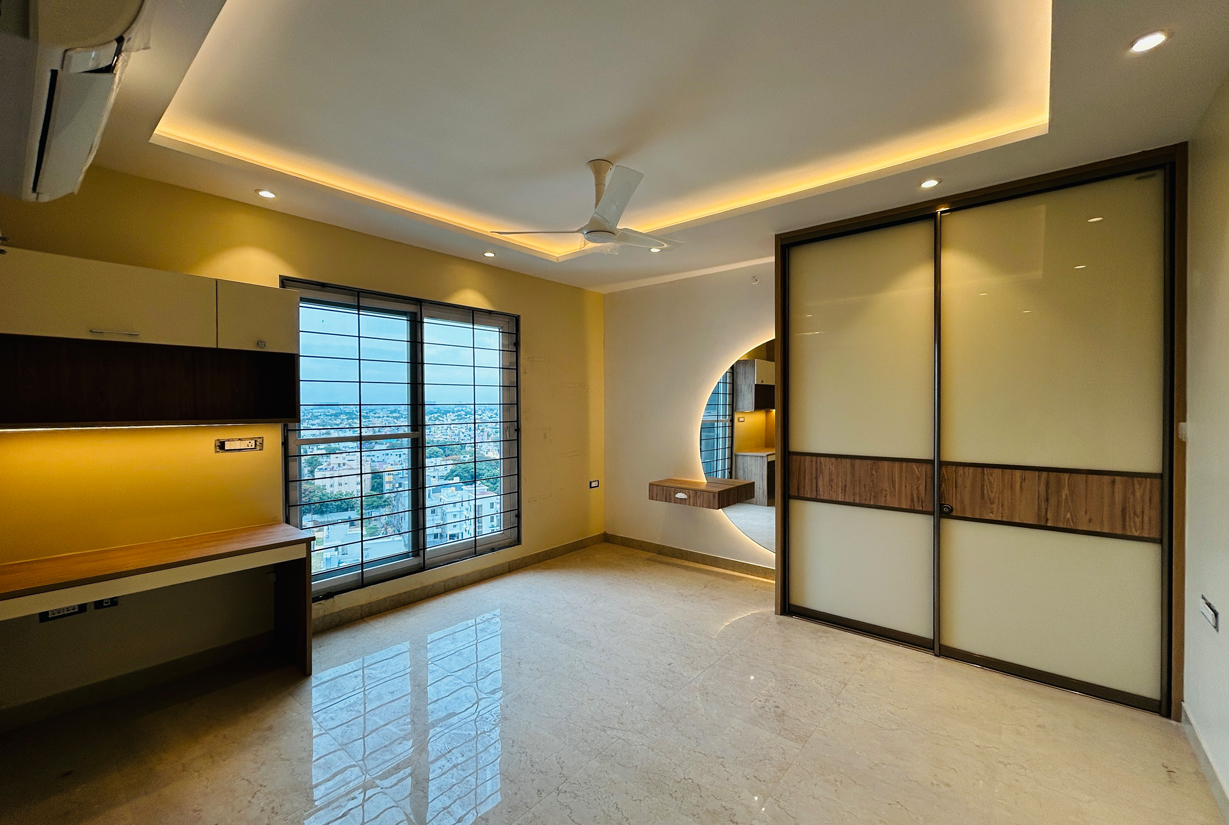 Spacious bedroom with integrated study desk, modern ceiling lighting,
						 and large windows with city view