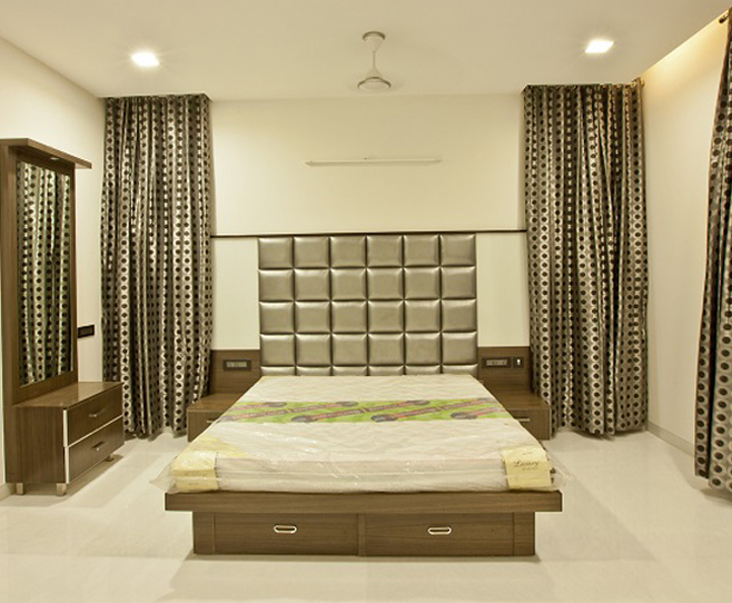 Minimalist bedroom with a large padded headboard,
								 neutral bedding, and modern bedside tables against floor-to-ceiling curtains.